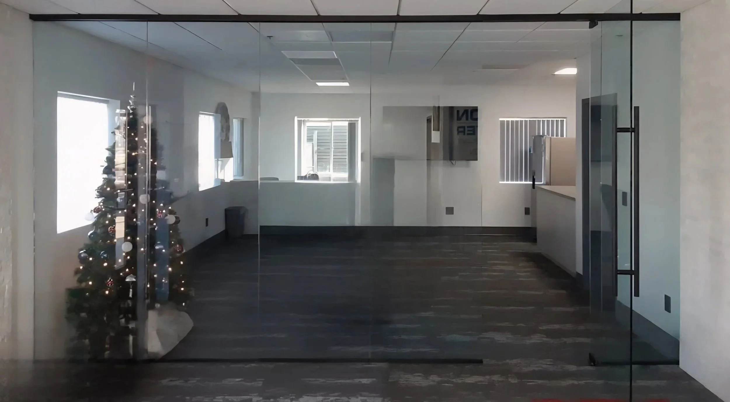 Empty office conference room with glass walls, a decorated Christmas tree, windows, and a reception counter with a monitor. glass divider. glass partition.