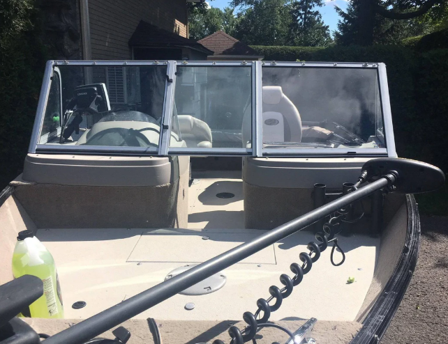 Front view of a beige motorboat with a clear windshield, a motor attached at the back, and a spray bottle on the left side, parked outdoors.