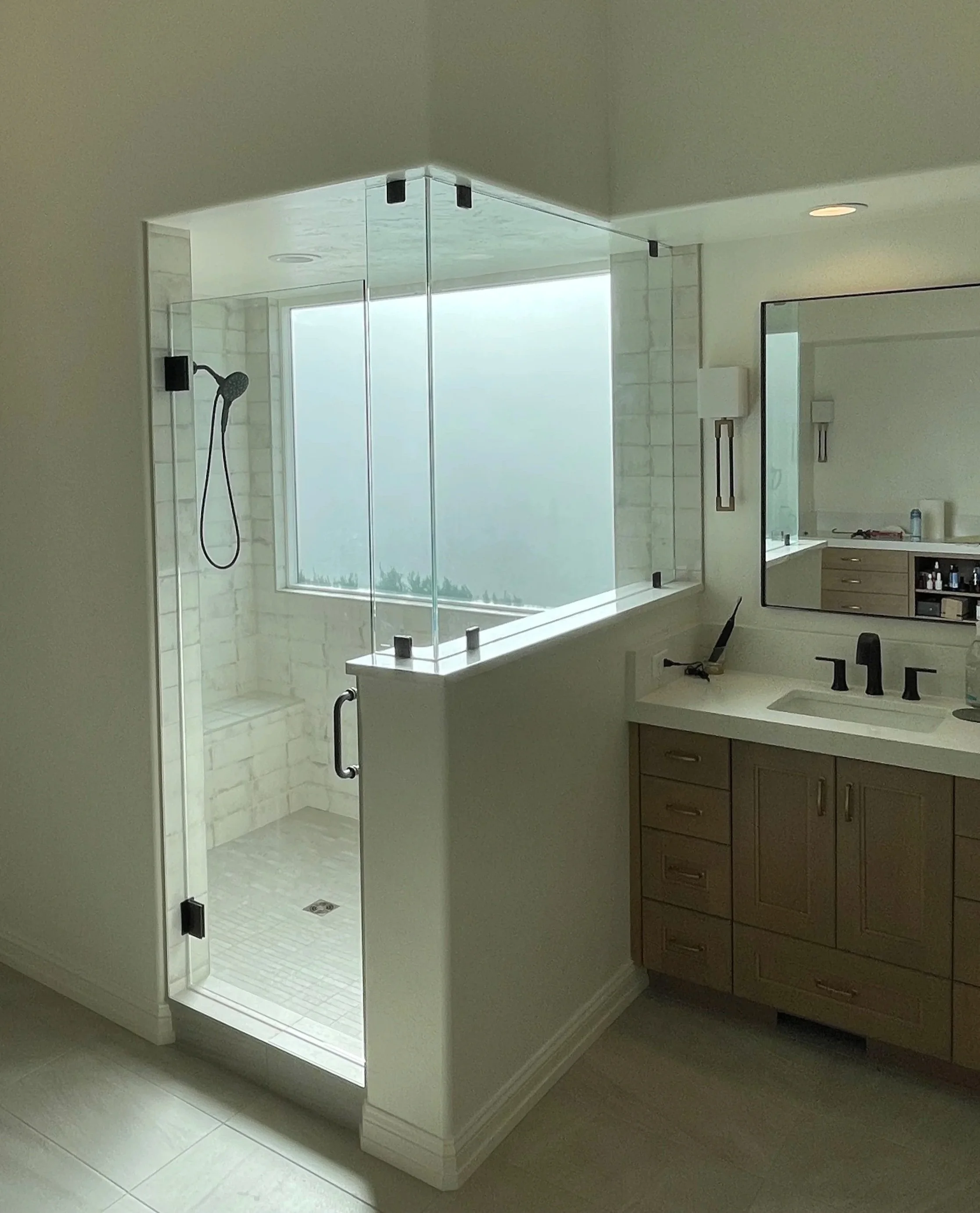 Modern bathroom with glass-enclosed shower, white tiled walls, and a vanity with a sink and mirror.