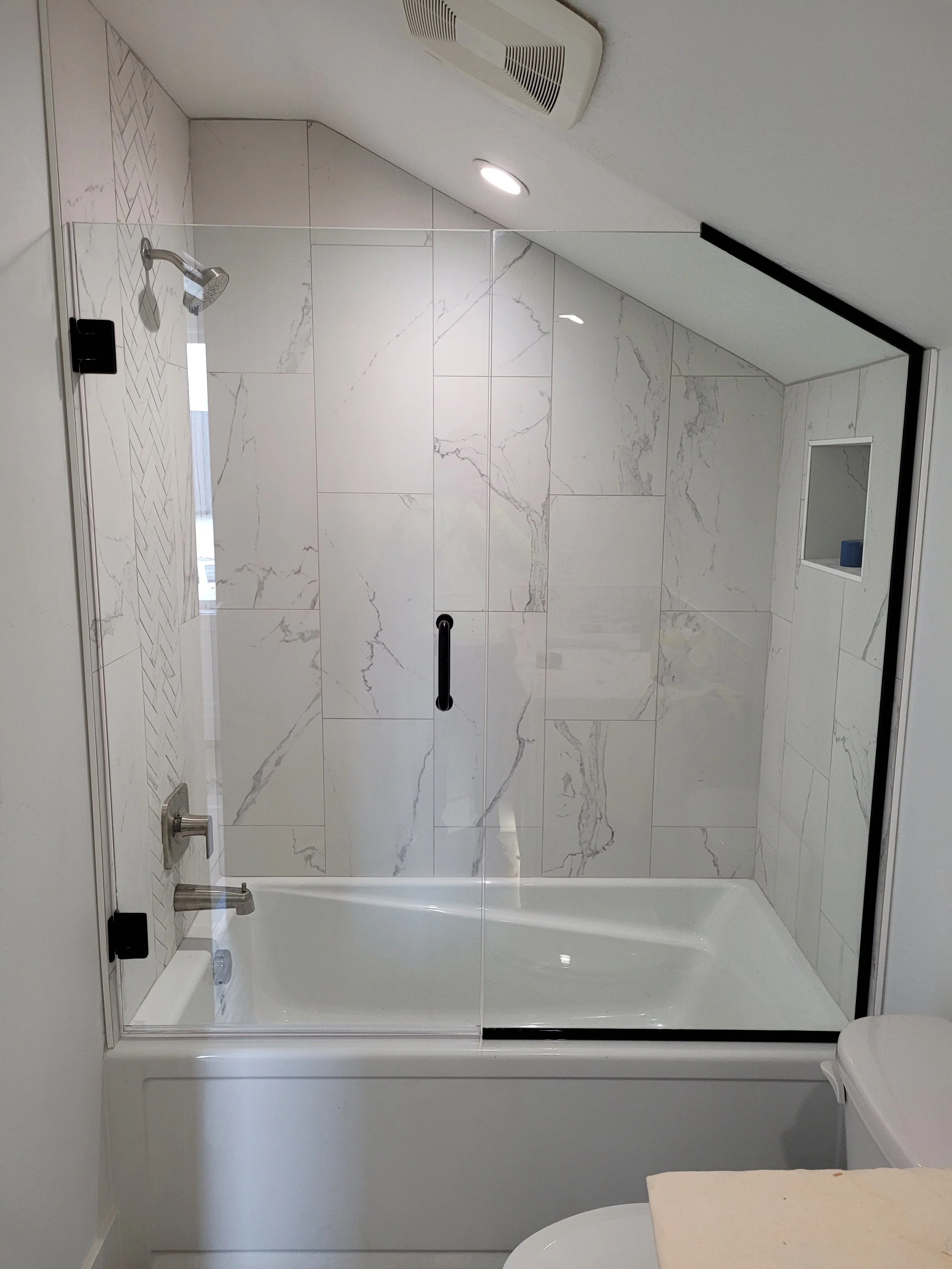 Modern bathroom with white marble tiled shower with glass door, small built-in shelf, and a ceiling vent.