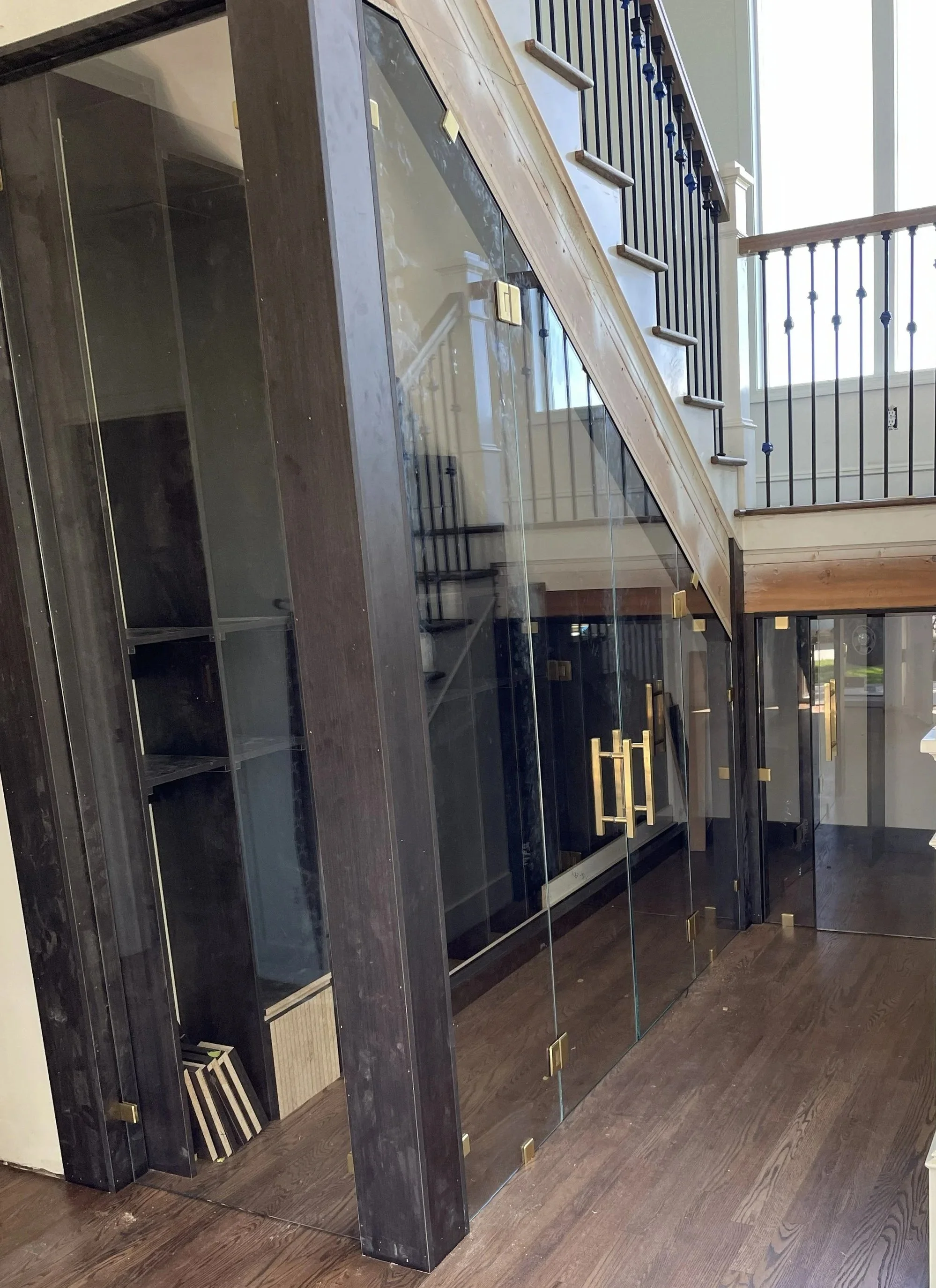 Interior view of a modern staircase with black metal railings and wooden steps, with glass wall panels and shelving underneath the staircase.