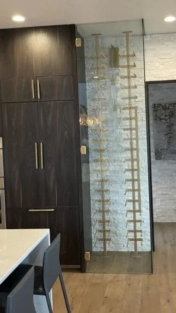Interior view of a room with a dark wood cabinet, a glass panel with a wooden wine rack, and part of a dining table with chairs. custom glass. glass wine cabinet. 