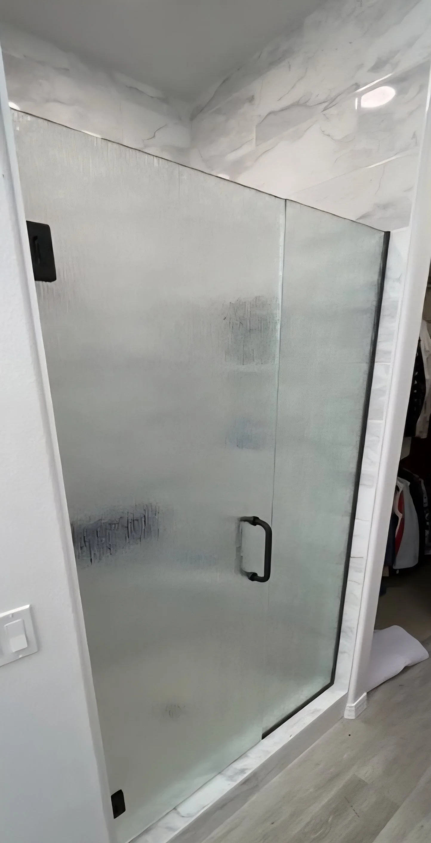 Bathroom shower with rain pattern glass door and black handle, surrounded by white marble tiles. u channel. custom shower. glass shower.