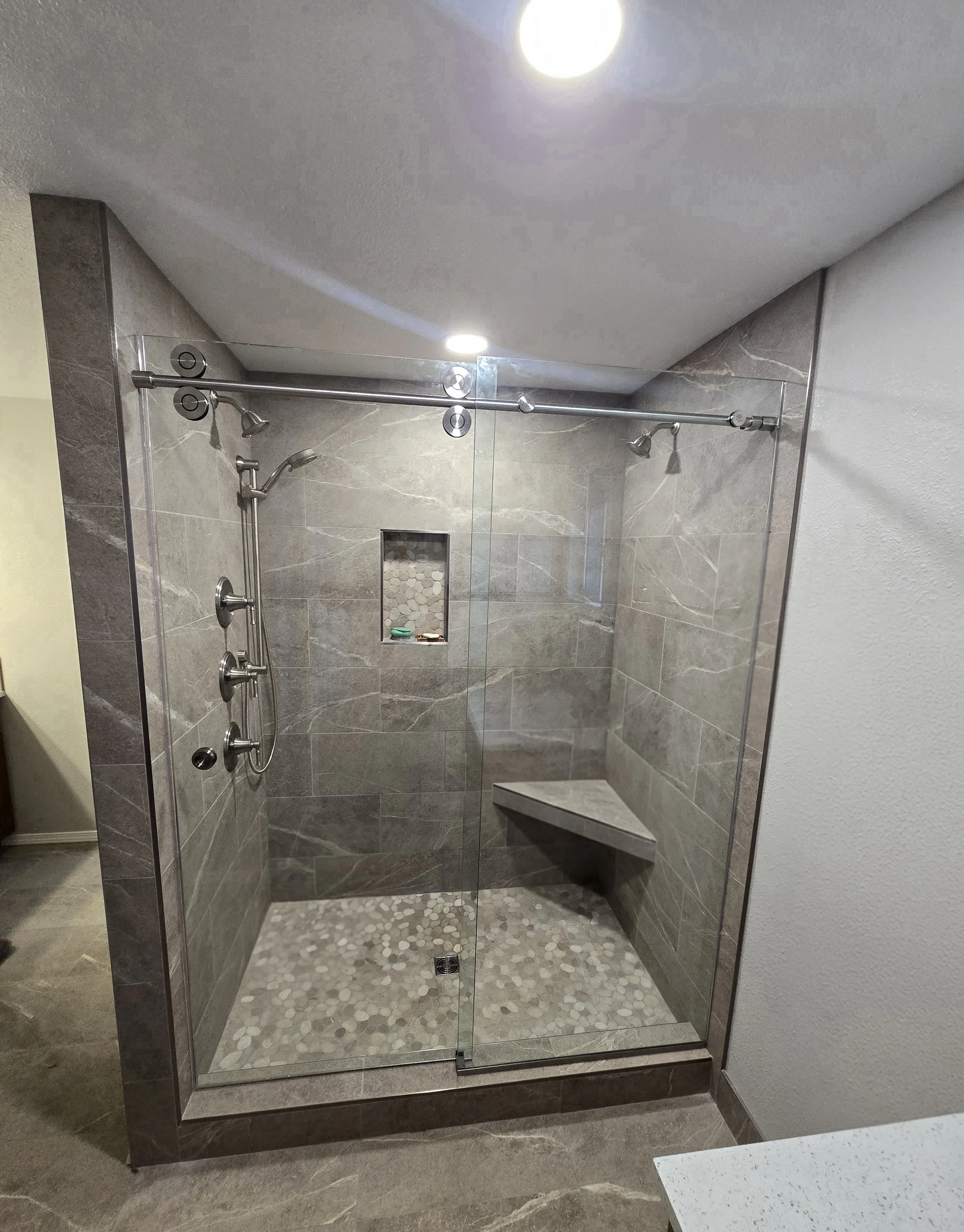 A modern, glass-enclosed shower with grey marble tiles, a built-in niche, and a bench.