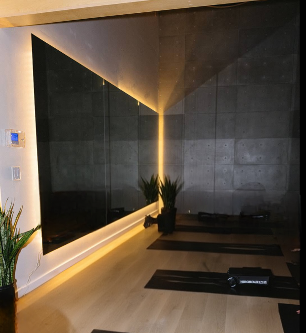 A modern interior room with a large mirror on the wall, potted plants, and yoga mats on a wooden floor.