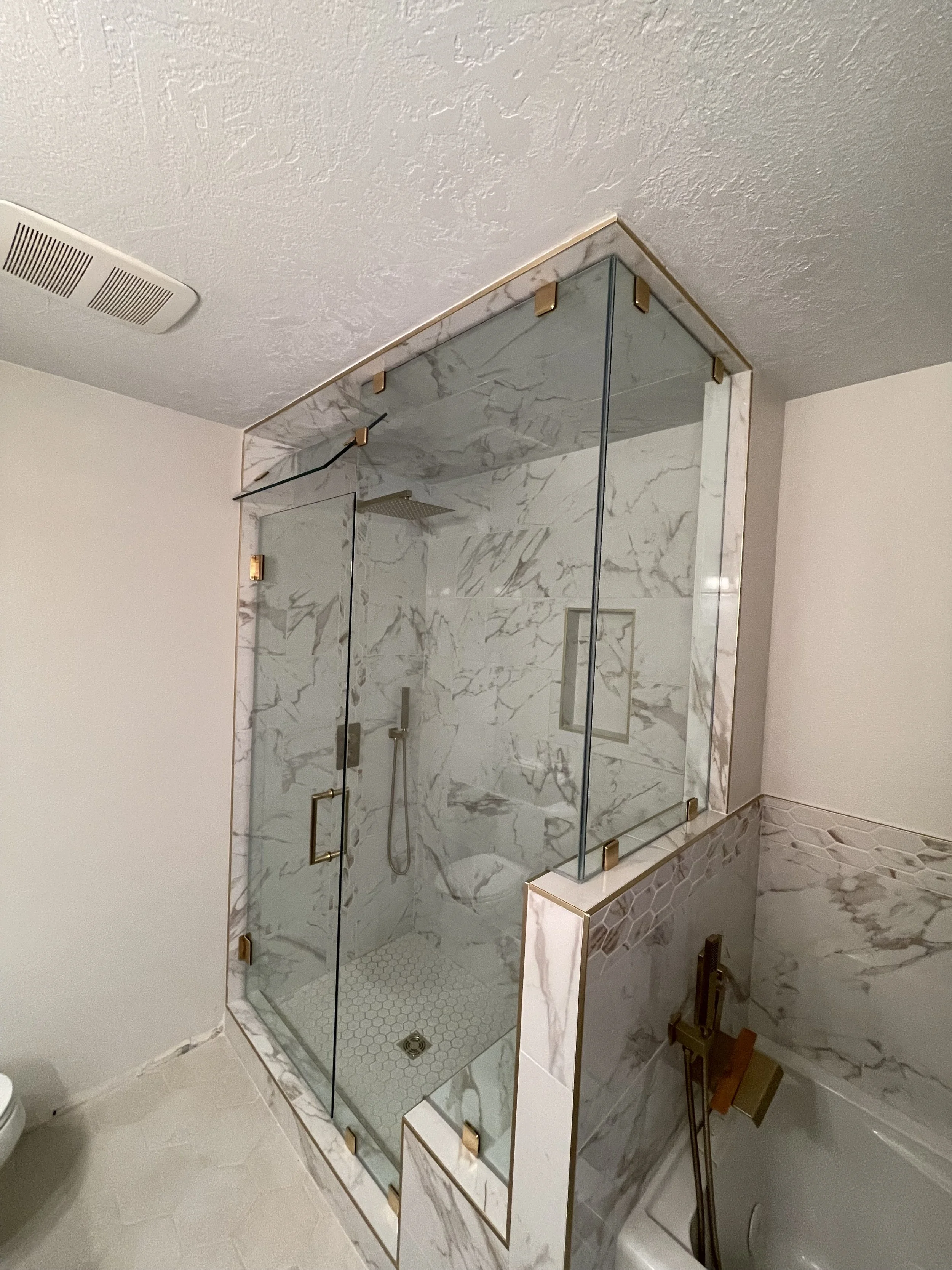 Marble shower enclosure with glass doors and gold hardware in a modern bathroom.