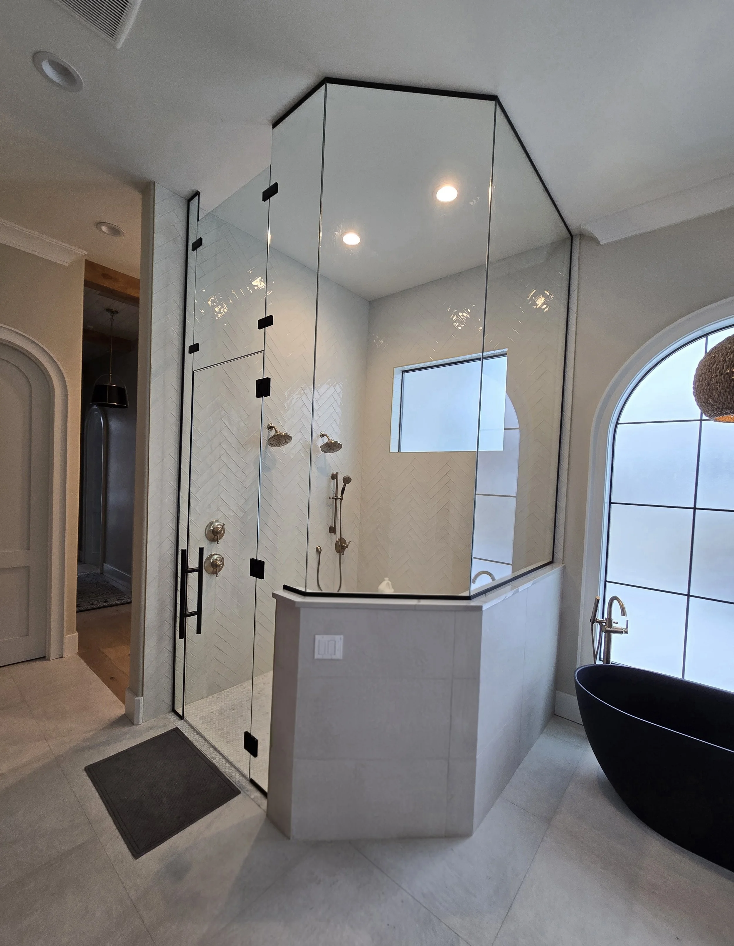 Modern bathroom with a black freestanding bathtub, glass-enclosed shower with dual shower heads, and large windows letting in natural light.