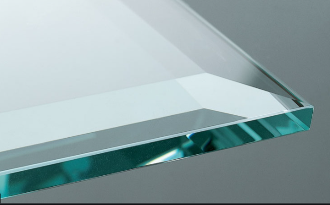 Close-up view of a clear glass or acrylic sheet with polished edges, resting on a gray surface.