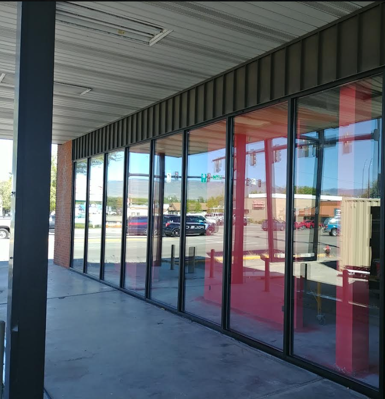 Empty storefront with large glass windows reflecting traffic and street view, over concrete sidewalk.