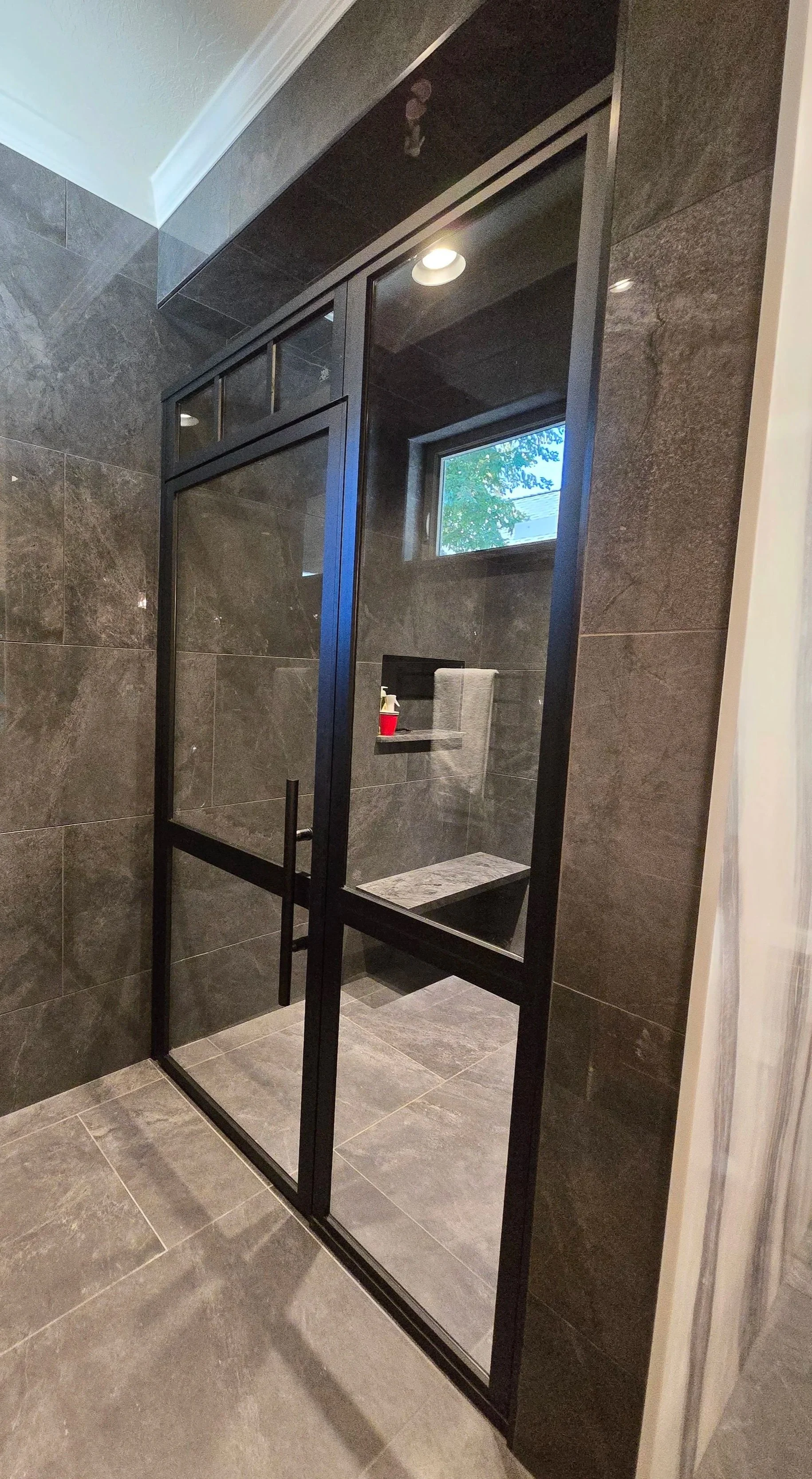 Modern shower with black-framed glass door and dark gray tile walls and floor.
