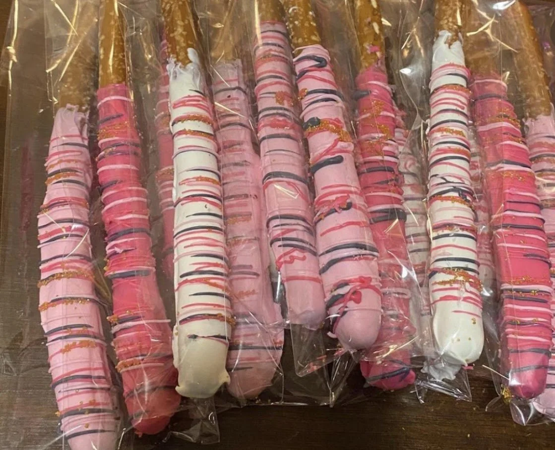 Collection of pink and white decorated pretzel rods wrapped in plastic.