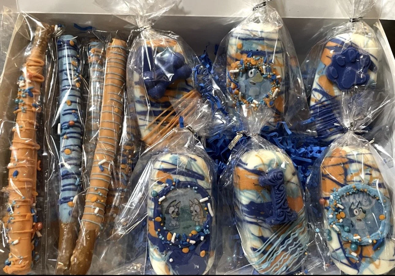 CAKE POPS decorated with blue, orange, and white icing, some featuring cartoon dog designs, all wrapped in clear plastic bags.
