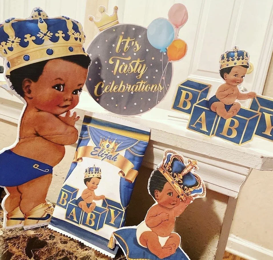 Decorations for a baby's celebration with images of a baby boy wearing a crown, blocks spelling 'BABY', balloons, and a sign that reads "It's Tasty Celebrations."