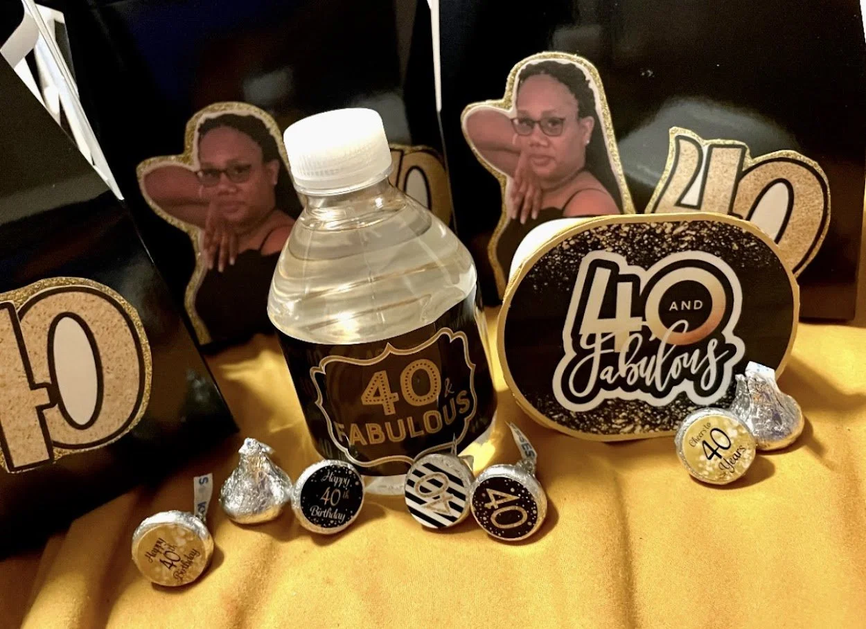 Decorative birthday celebration setup with black and gold themes celebrating a 40th birthday, featuring signs, candies, and a water bottle.