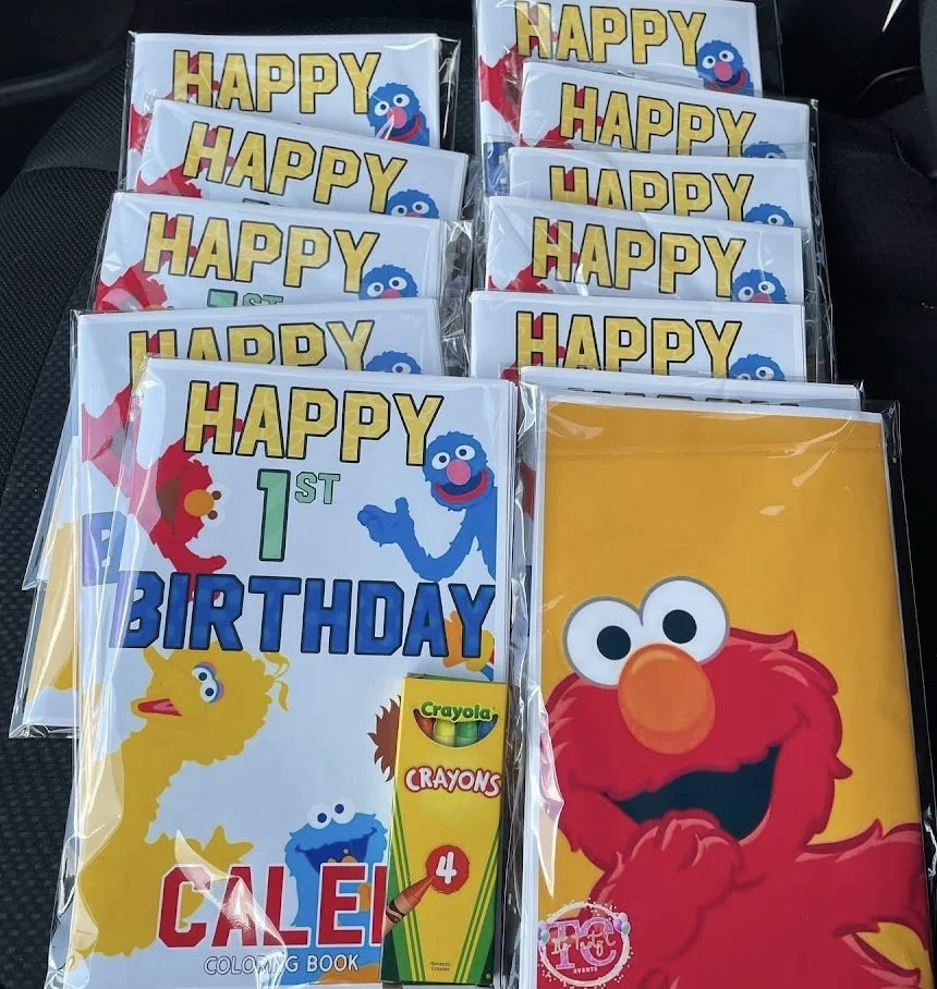 Multiple copies of Sesame Street-themed birthday party supplies featuring Elmo and other characters, including a coloring book, a large poster, and a pack of Crayola crayons, all celebrating a 1st birthday.