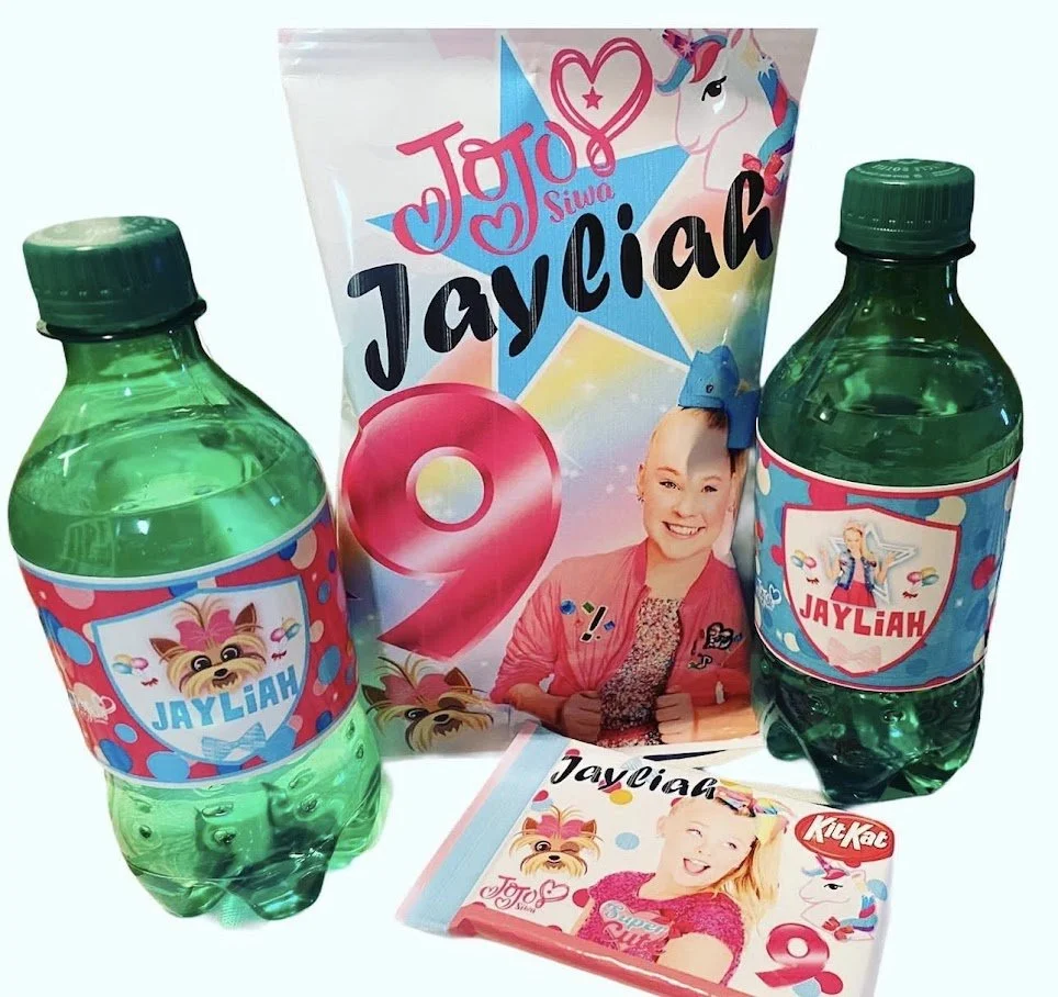 Collection of JayaLiah themed birthday party items including two green soda bottles with custom labels, a party favor bag with a girl and unicorn graphic, a notebook, and a small container, all featuring bright colors and decorative graphics.
