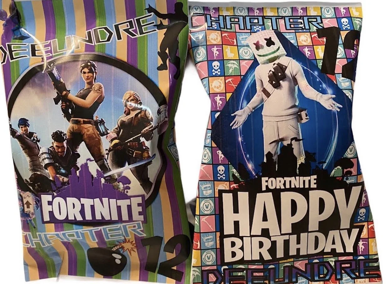 Two Fortnite-themed gift bags, one with a group of four characters in action poses and colorful striped background, and the other with a single character wearing a marshmallow head and a birthday message, both featuring Fortnite branding and vibrant,