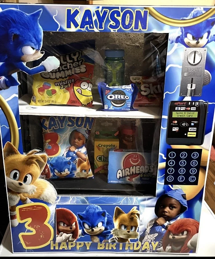 A Sonic the Hedgehog-themed vending machine with a glass front showing various snacks, including Oreo cookies, Fruit Snacks, and airheads, decorated with Sonic characters and a message that says "Happy Birthday".