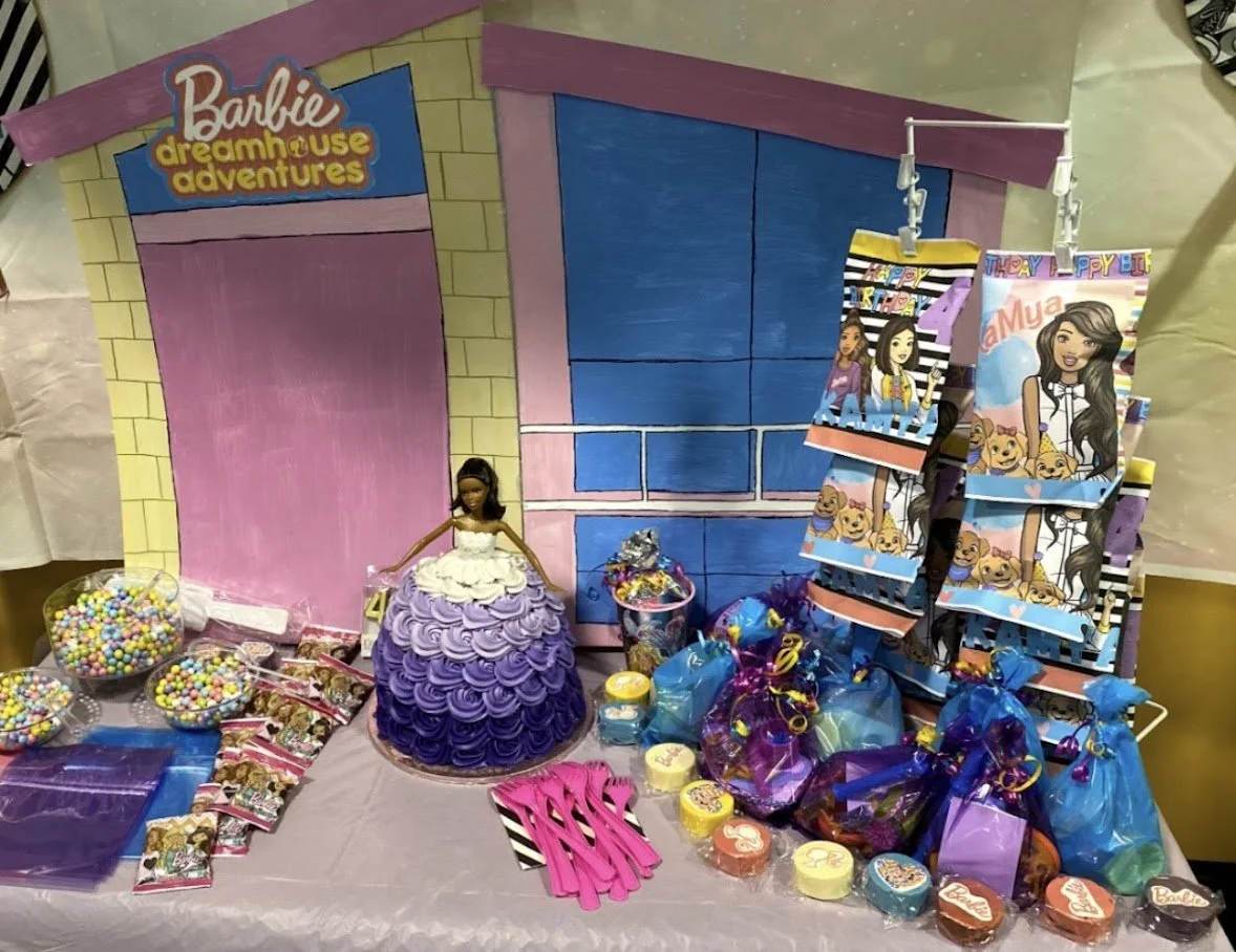 Barbie Dreamhouse Adventures themed party setup with a cake, candy, party favors, and decorations featuring a pink and blue house background.