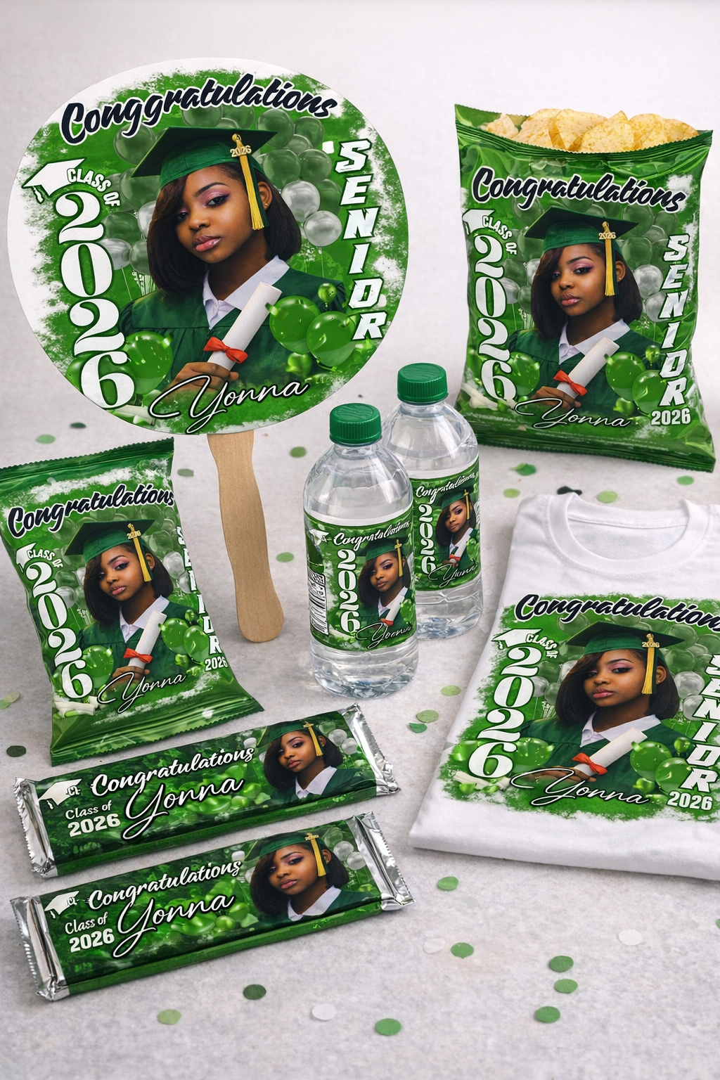 Graduation-themed party favors featuring a girl in a green cap and gown holding a diploma, with the text 'Congratulations Class of 2026 Yonna' on various items including a sticker, popcorn bag, water bottles, and a T-shirt, all decorated with green a