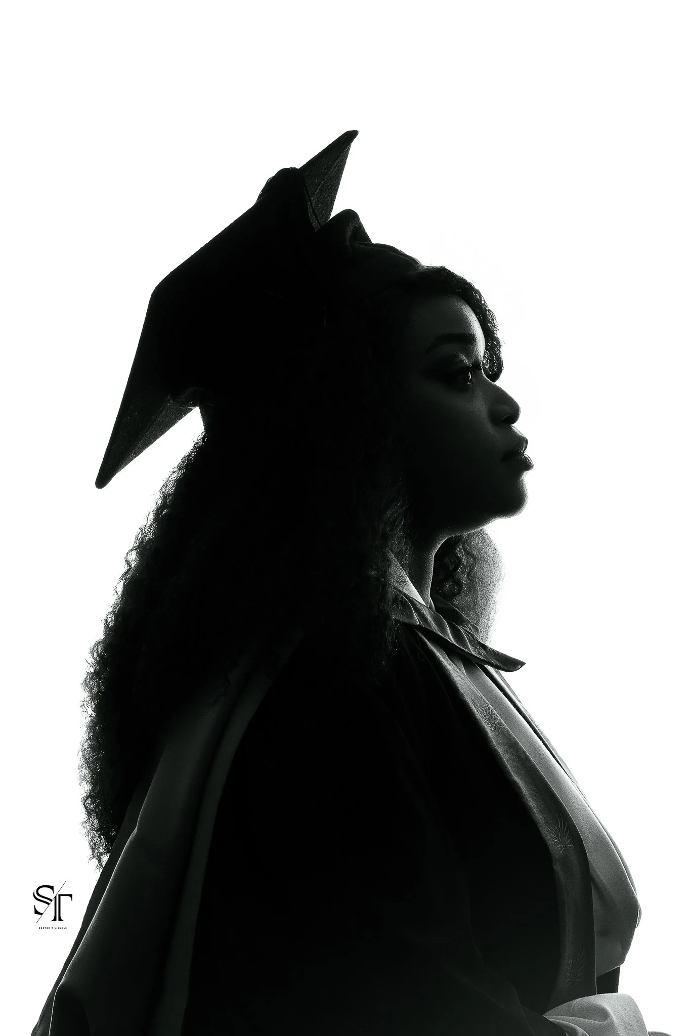 Silhouette of a woman with curly hair wearing a graduation cap, facing to the right, in front of a white background.