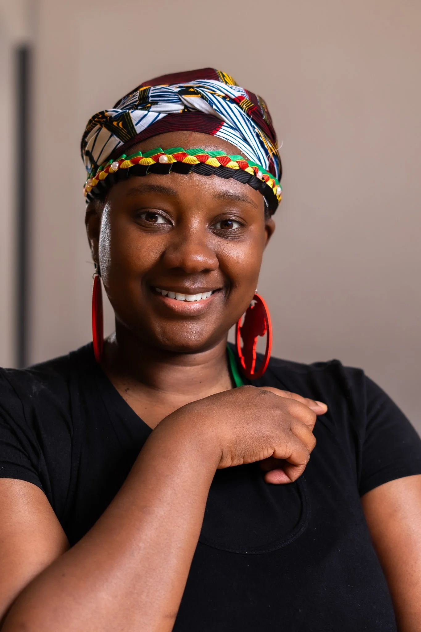 A smiling woman wearing a colorful headwrap, red earrings, and a black shirt.