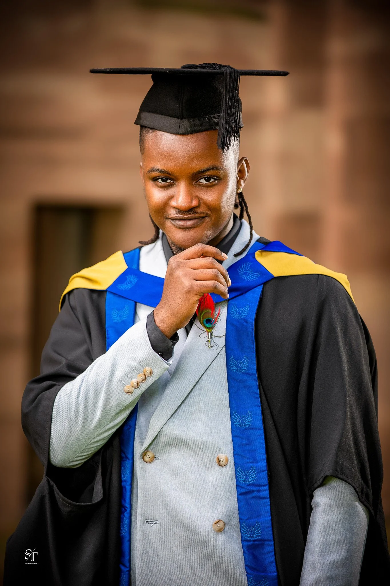Young man in graduation gown and cap, standing outdoors with a confident smile.