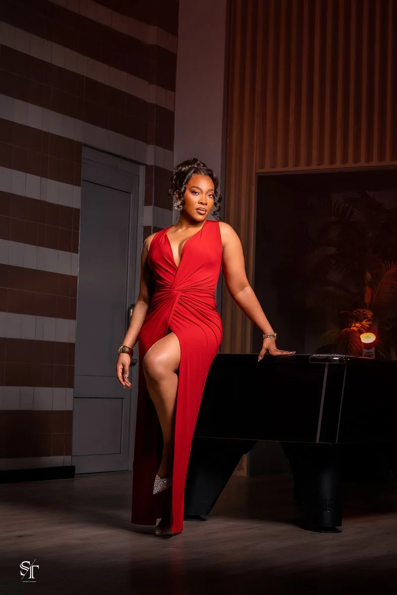 Woman in a red evening gown standing next to a black grand piano in a modern interior setting.