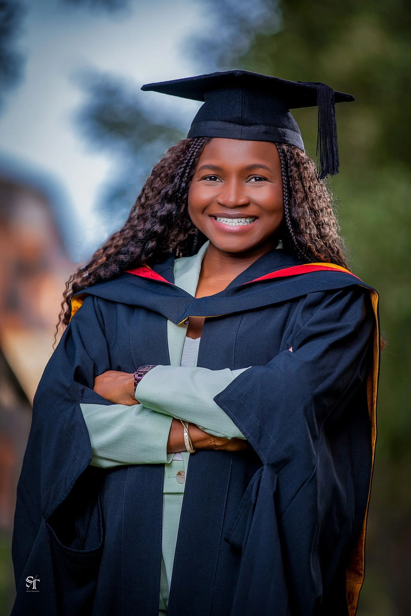 A young woman in graduation cap and gown smiling outdoors.