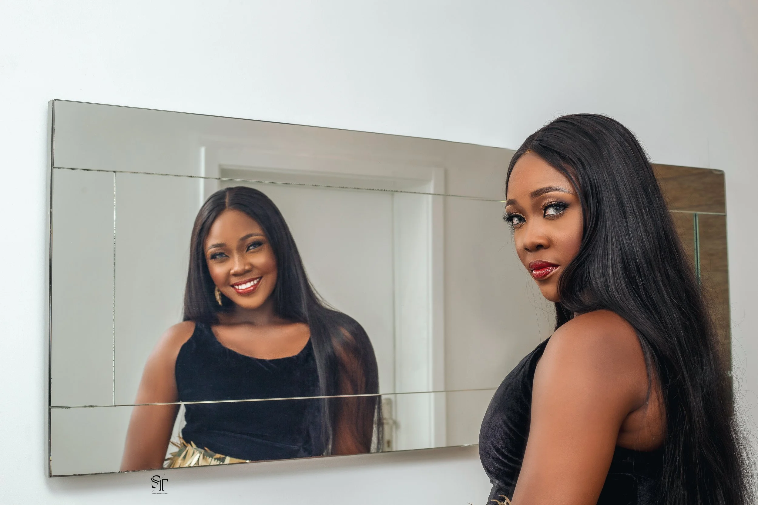 A woman with long dark hair and makeup looking at a mirror with a happy expression