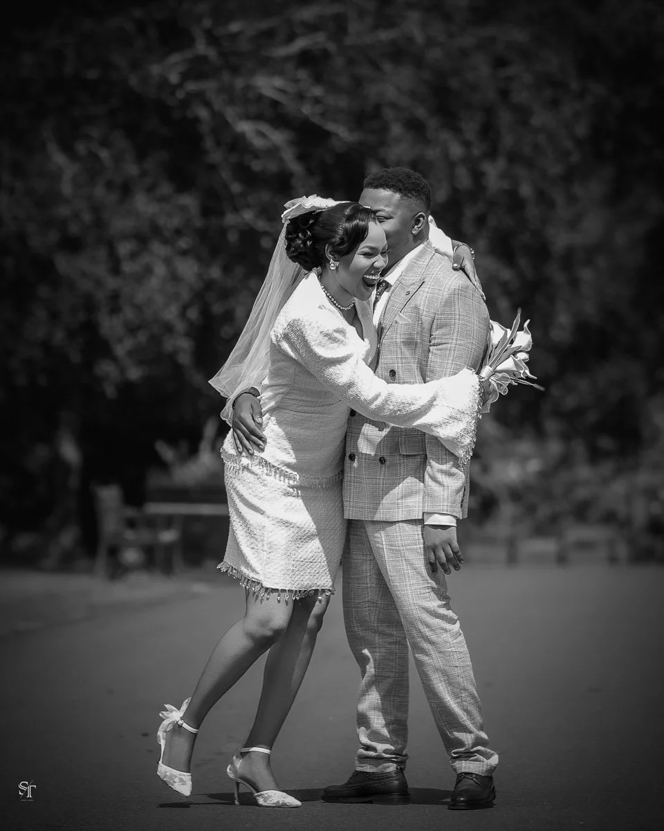 A black and white photo of a bride and groom sharing a joyful moment outdoors, with the bride laughing and embracing the groom.