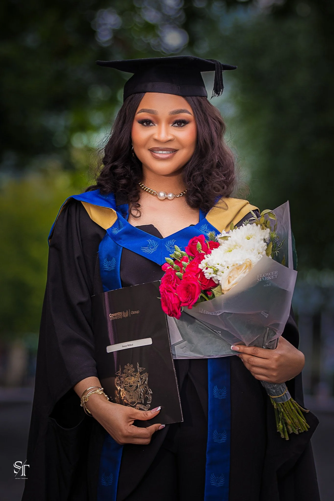 A woman in a graduation cap and gown holding a bouquet of red and white flowers and a diploma at outdoors during the daytime.