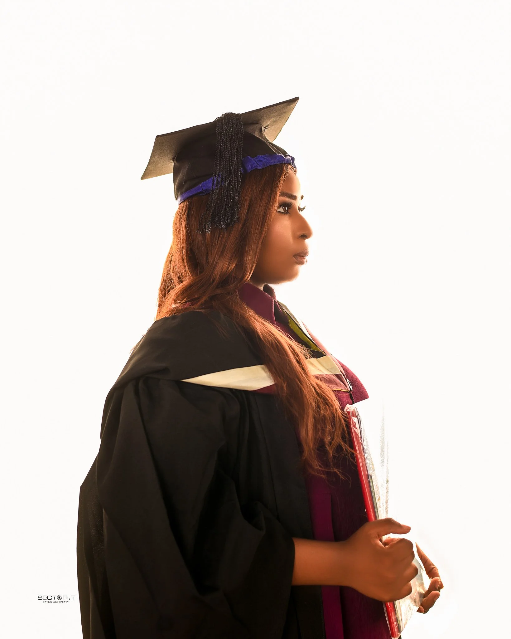 Young woman in a graduation cap and gown holding a diploma, in profile view.