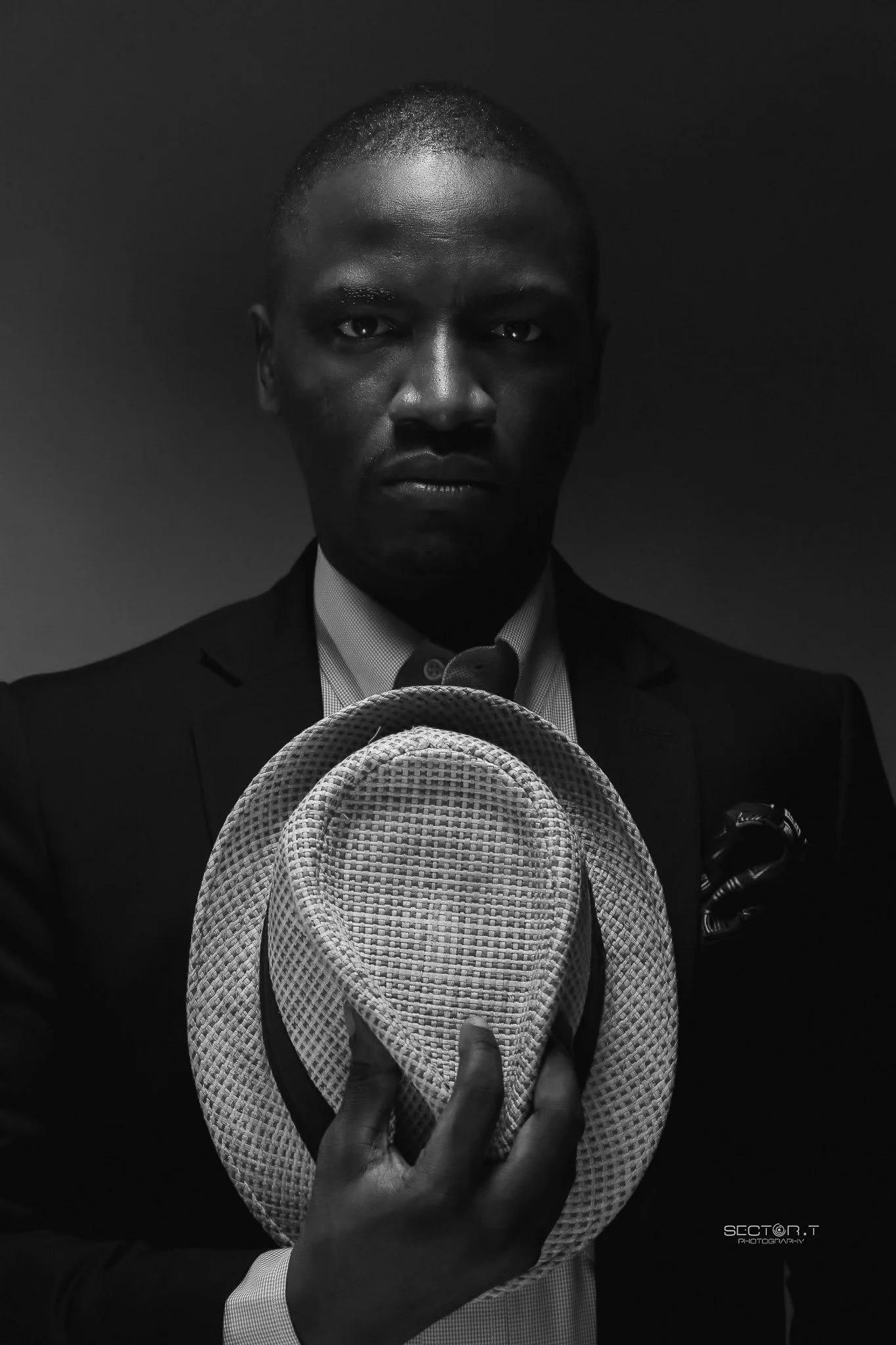 A black man in a suit holding a fedora hat, with a serious expression on his face, in black and white.