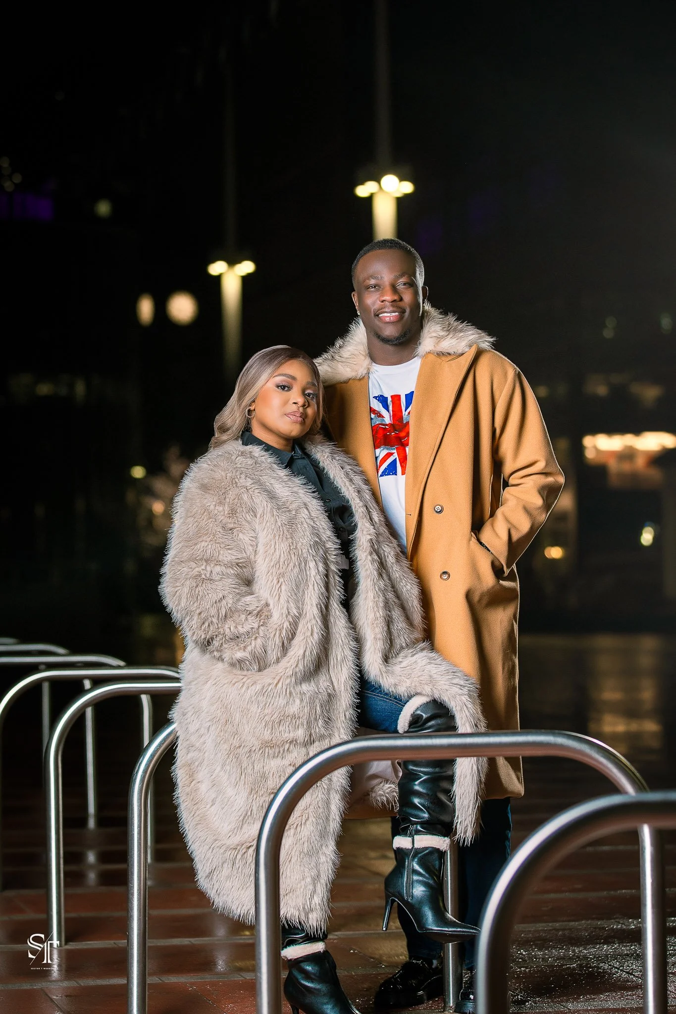 A man and woman dressed in fashionable winter clothing posing outdoors at night.