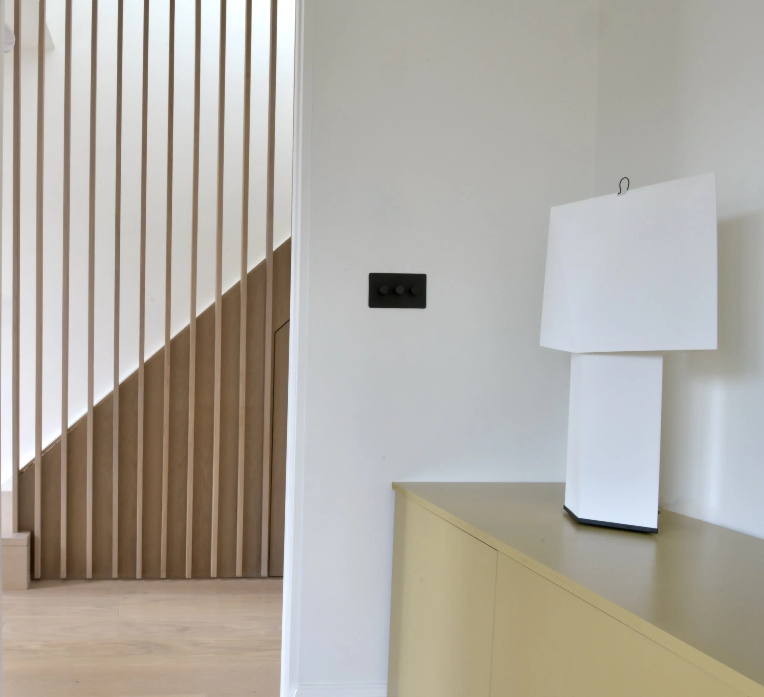 Interior view of a modern room with wooden slat wall, yellow cabinet, white table, and a white lampshade.