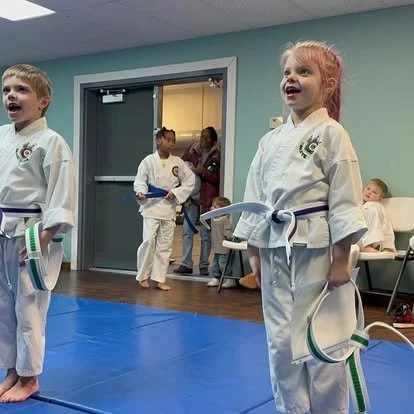 Kids in martial arts uniforms standing on a mat during class.