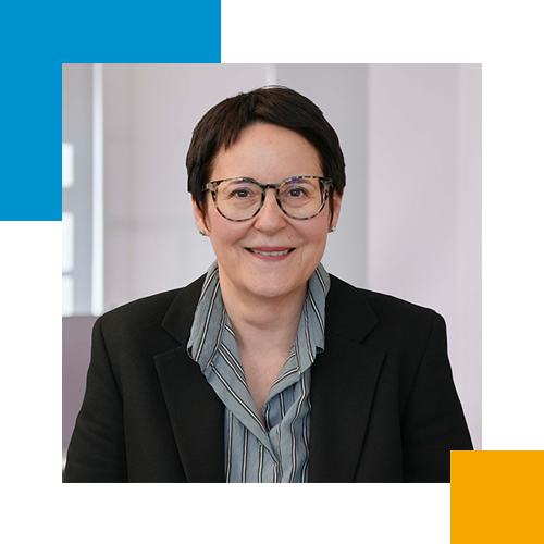 Porträt einer Frau mit Kurzhaarfrisur und Brille, die in einem professionellen Umfeld lächelnd in die Kamera schaut.