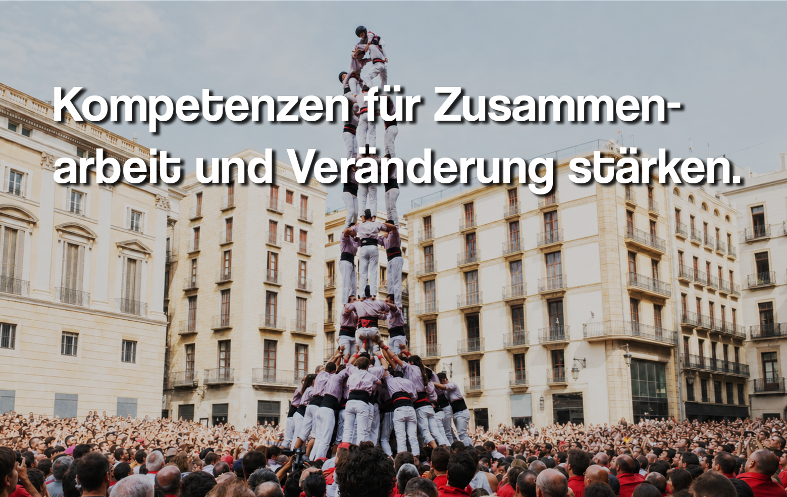 Ein großer Menschenturm, aufgebaut aus mehreren Ebenen, im Stadtzentrum mit vielen Zuschauern. Der Text auf dem Bild lautet: "Kompetenzen für Zusammenarbeit und Veränderung stärken."