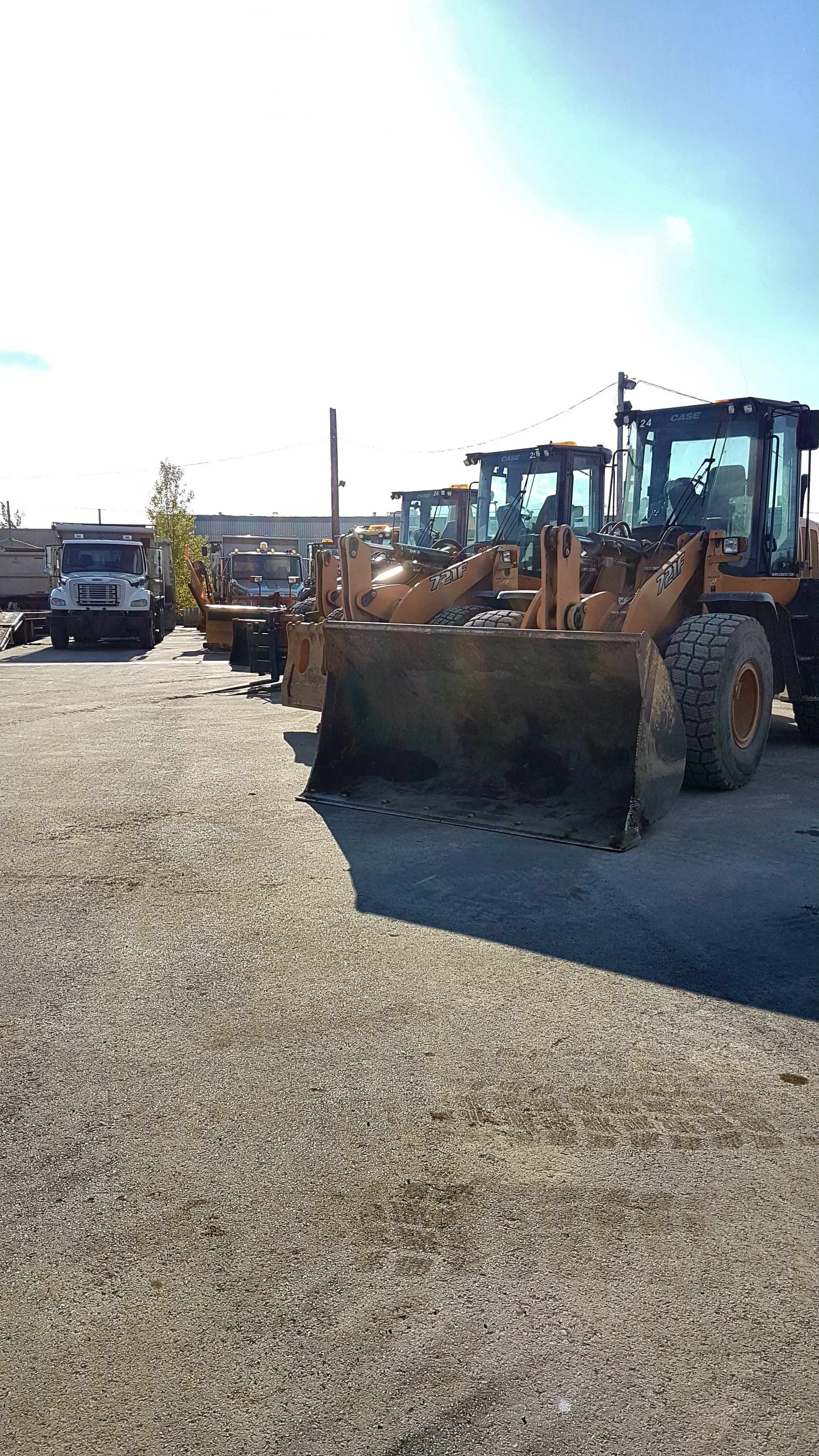 Une rangée de pelleteuses et d'autres véhicules de construction stationnés dans une zone de travail extérieure.