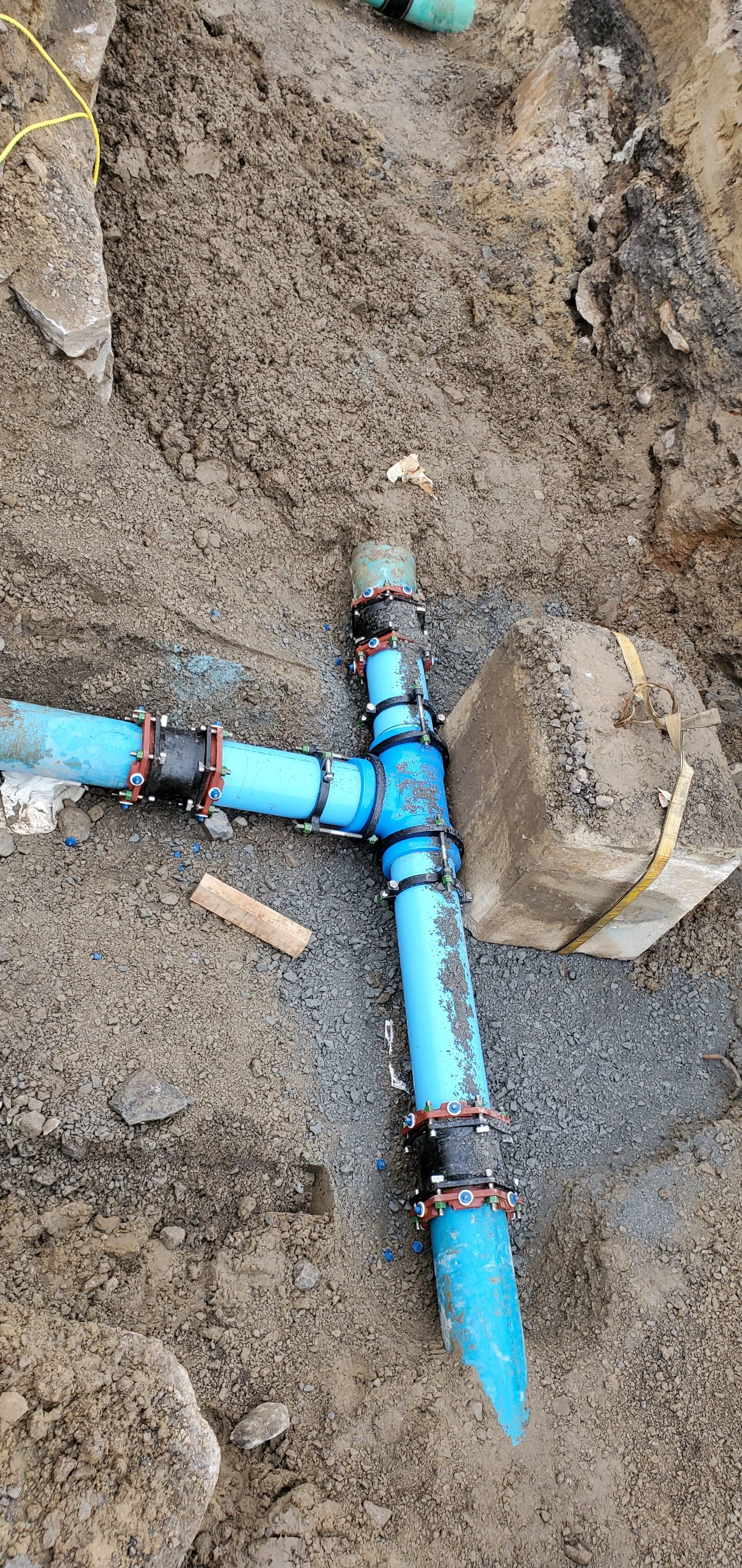 Pose de tuyaux en plastique bleu dans une tranchée avec des raccords, entourée de terre excavée.