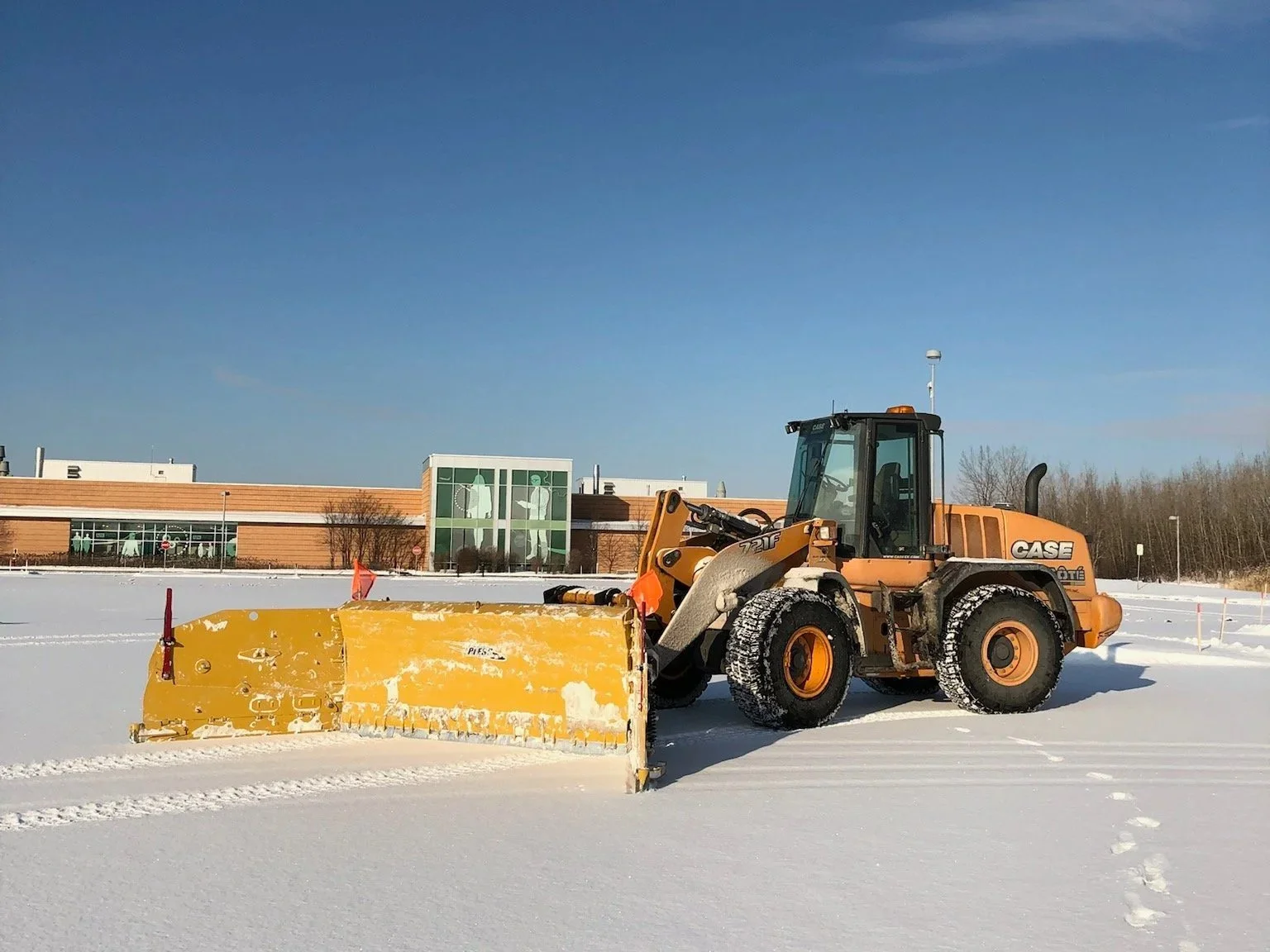 Un bulldozer orange de la marque CASE en train de déneiger une surface enneigée.