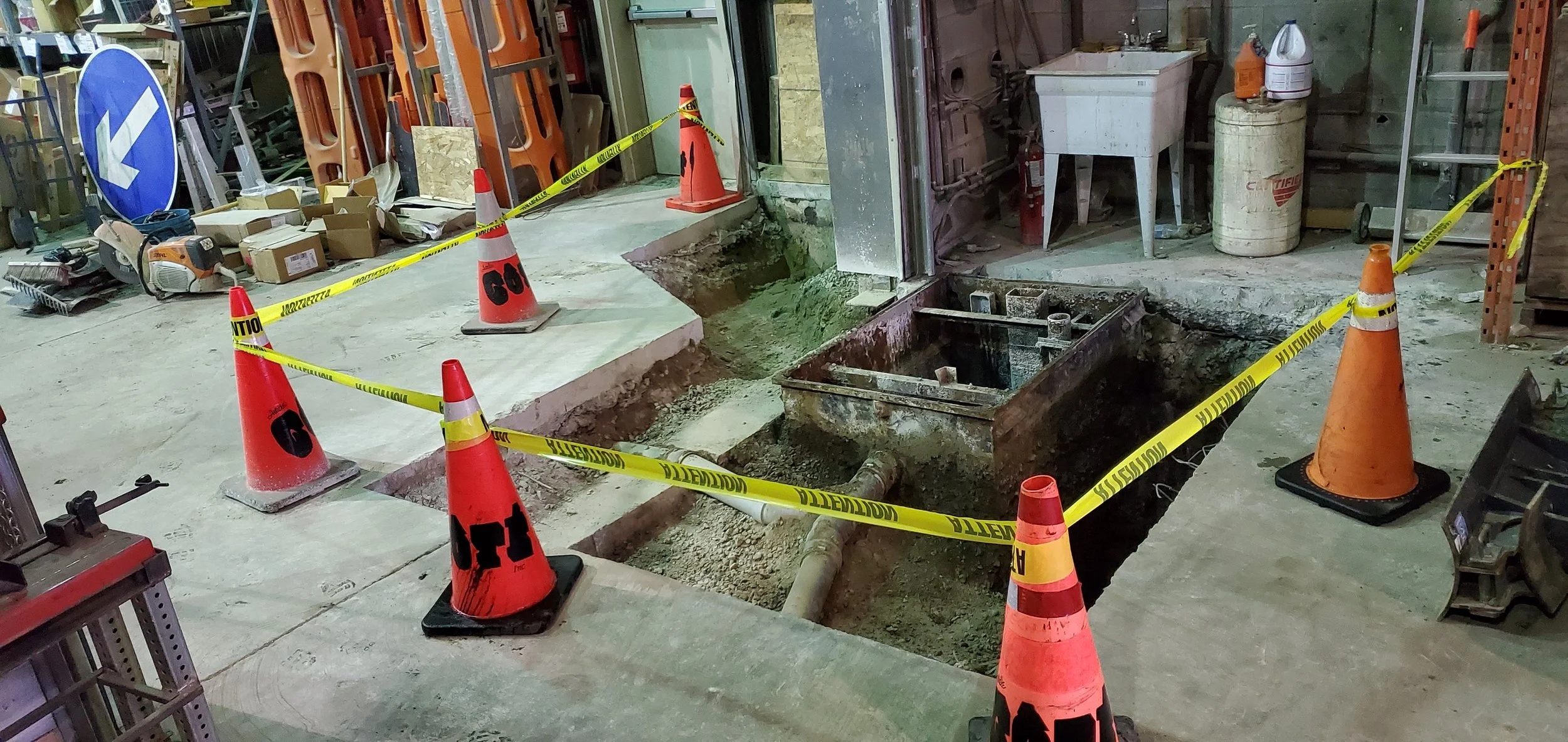 Travaux de réparation ou excavation dans un atelier ou garage, avec des cônes de signalisation, du ruban de sécurité jaune et du sol en travaux.