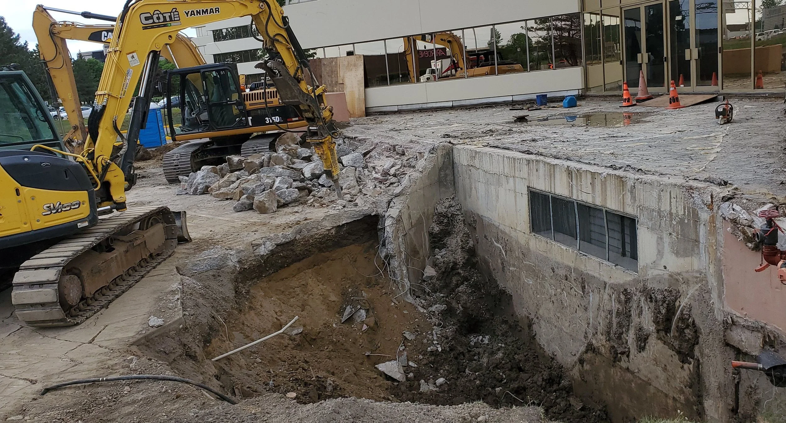 Ouvrage de travaux de construction avec une excavatrice jaune en action, creusant une ouverture dans le sol, entourée de débris et de matériaux de construction, dans un environnement urbain