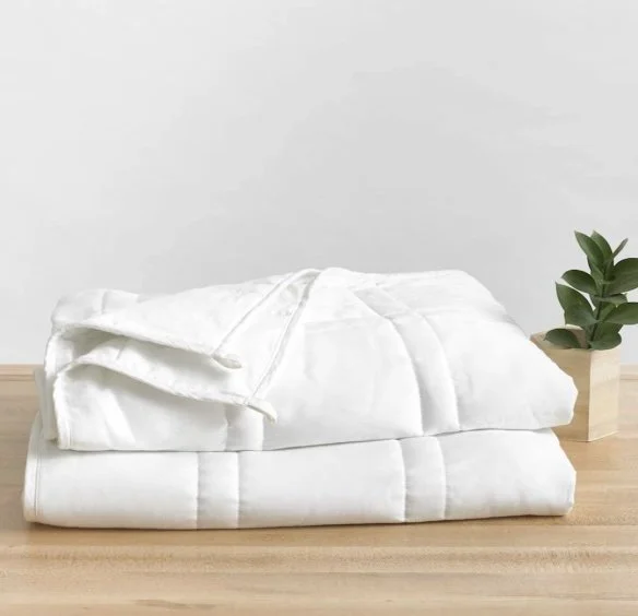 Stacked white towels or robes on a wooden surface with a small potted green plant nearby.