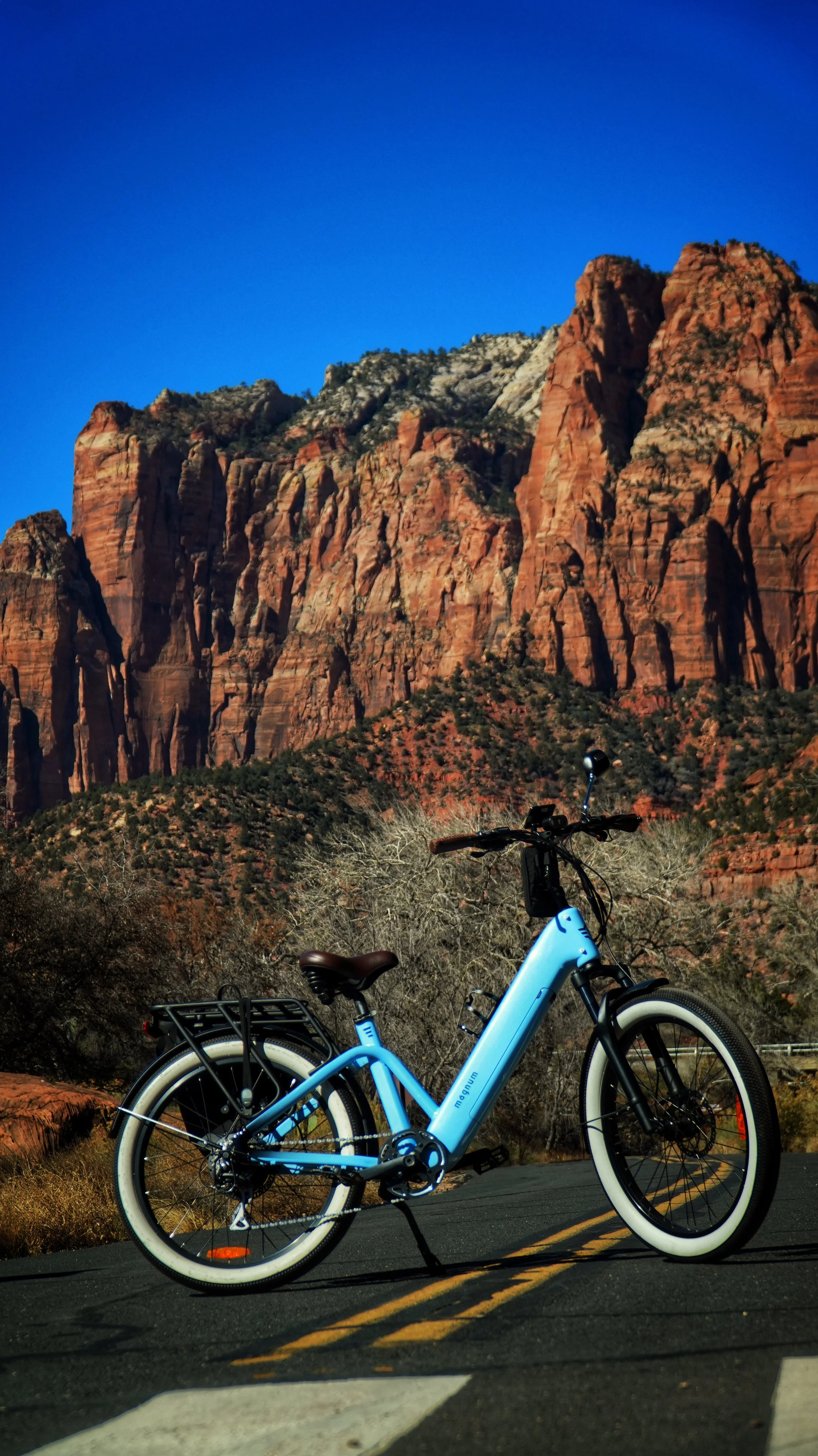 A blue electric bicycle parked on a road in front of red rock formations and a clear blue sky.
