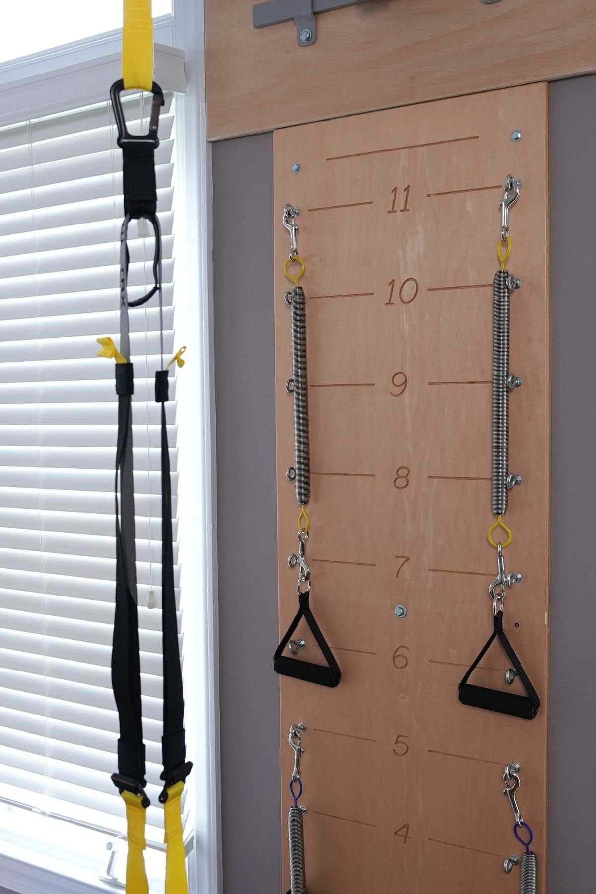 Workout equipment including black and yellow suspension straps hanging beside a wooden wall mounted pegboard with metal springs and hooks.