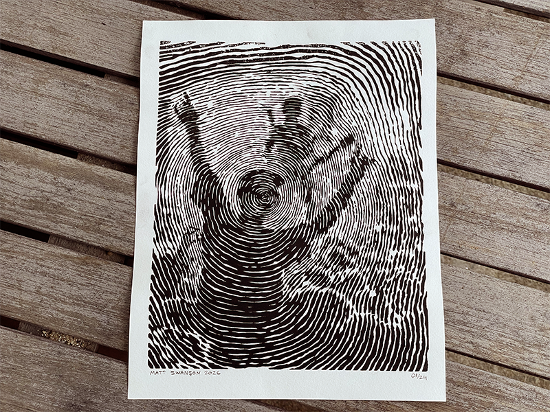 Photograph of a black and white linocut art print featuring a person crowd surfing at a concert, drawn in a continuous spiral design, made by Matt Swanson