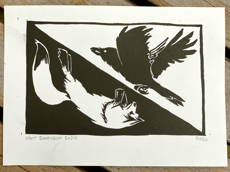 Photo of a black and white linocut art print featuring an arctic fox and a raven chasing each other in a sort of yin-yang arrangement, made by Matt Swanson