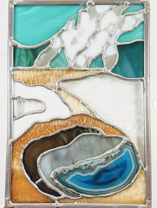 A blue agate placed in the middle of a stained glass piece that looks like a geyser pool in Yellowstone National Park. 